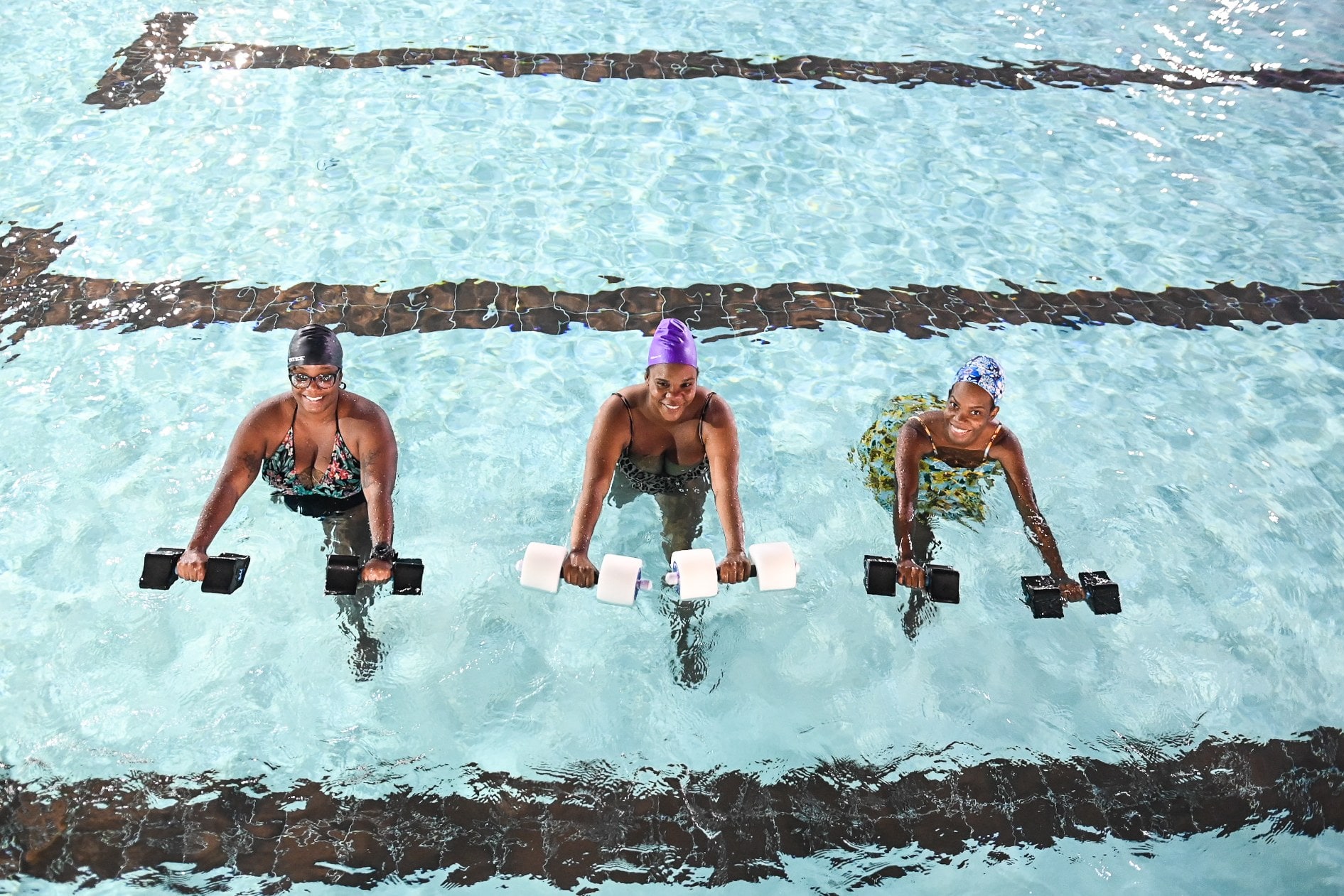 Three women using water dumbbells during an AquaAerobics class in the pool
